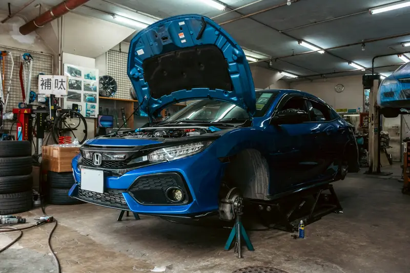 Honda Civic récente sur chandelles, capot ouvert, dans un atelier de mécanique